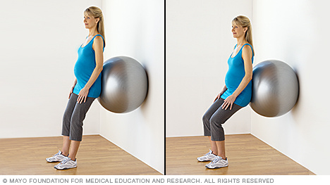 Pregnant person doing squats with a fitness ball